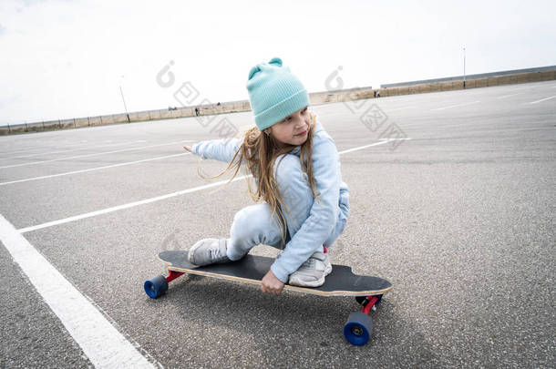 街头运动：一个穿着蓝色毛衣和帽子的女孩在长板上快速滚动.