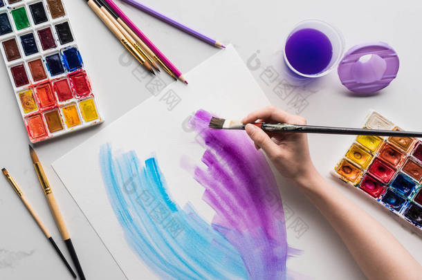 艺术家在大<strong>理石</strong>白色表面上的白纸上绘制紫色和蓝色水彩笔触的裁剪视图