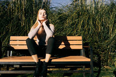 迷人的美丽年轻的金发模特女孩坐在一个长凳上户外, 享受太阳和摆姿势