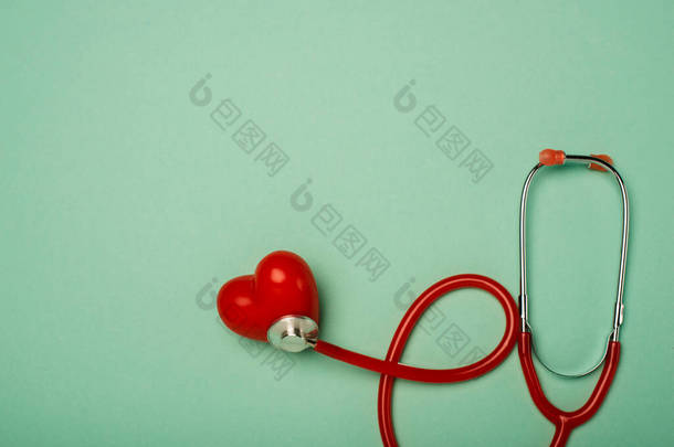 绿色背景下与装饰红心相连的听诊器的顶视图，世界卫生日概念
