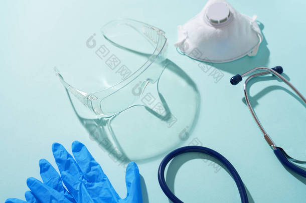 蓝色背景的听诊器、呼吸器、医用手套和防护眼镜.