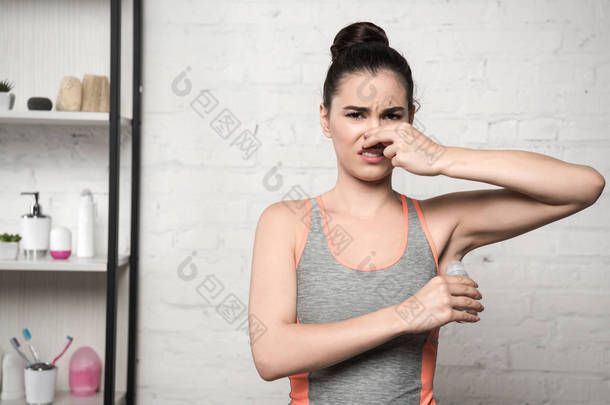 妇女在腋下涂除臭剂时，用手塞住鼻子感到震惊
