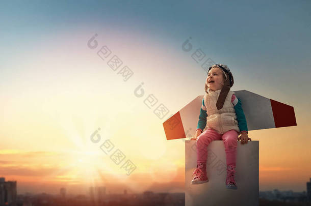 小孩子在当飞行员。女孩在日落天空的背景。穿着宇航员服装梦想成为一名太空人的孩子.