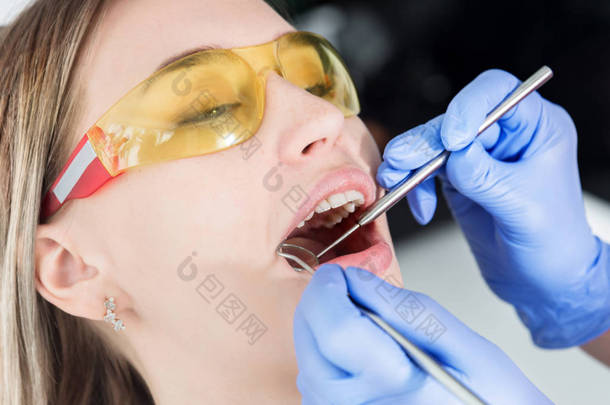 一名牙科检查人员张着嘴，<strong>闭</strong>着餐巾和<strong>眼睛</strong>，检查了这些女孩的面部特写镜头。牙医手与检查工具