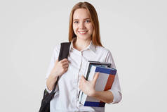 回到学校的概念。微笑的欧洲女学生穿着高雅的衣服, 背着背包和成堆的书, 很高兴有周末经过漫长疲惫的一周的学习, 与世隔绝的白色背景