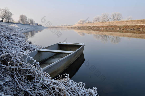 冬天被遗弃的船停泊在河岸上.平静的河流，早晨，阳光和霜冻.