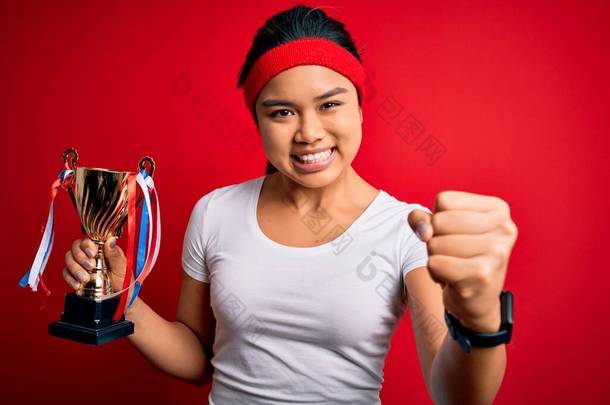 年轻的冠军亚细亚女子赢得奖杯站在孤立的红色背景上愤怒地大叫，疯狂地高喊，怒气冲冲