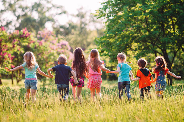 在阳光明媚的夏日，一群身穿休闲装的孩子、朋友、男孩和女孩在公园里奔跑 .