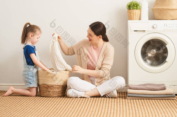 在家里洗衣服的时候，漂亮的年轻妇女和小女孩的小助手们都在开心地笑着.                                