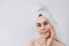 皮肤护理。一个美丽和微笑的女人使用护肤品, 润肤霜或化妆水照顾她的干肤色。把润肤霜涂在她脸上。文本的位置