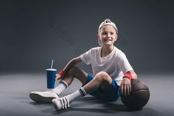 <strong>微笑</strong>青春期前男孩与苏打饮料和篮球球灰色背景