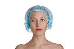 一个戴着蓝色医疗帽的漂亮姑娘，背景是白色的、与世隔绝的。 美丽的年轻女子，皮肤清澈。 面部治疗。 化妆品，美容和温泉。 护肤、面部特写