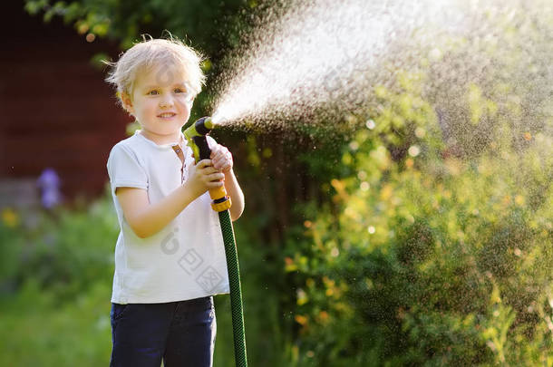 <strong>在</strong>阳光明媚的后院玩花园软管的滑稽小男孩。学前儿童玩喷雾水的乐趣。儿童夏季户外活动.