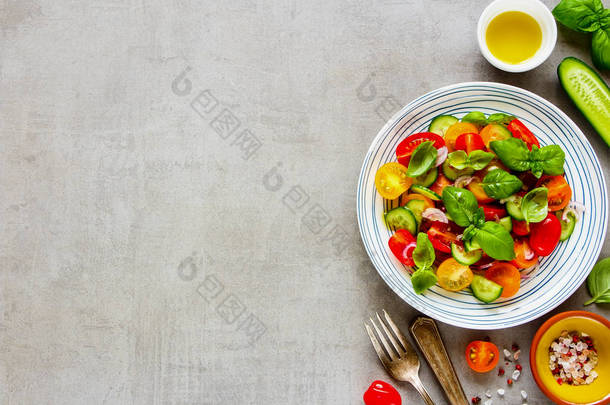 健康的彩色沙拉在板材和成分的光背景从上面。新鲜樱桃西红柿, 黄瓜, 红洋葱, 橄榄油, 罗勒和香料平躺.