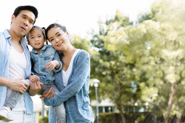 在<strong>暑假</strong>期间，亚洲家庭的父亲、母亲和女儿在公园里开心地笑着。每个人都穿着蓝色衬衫。拥抱对方<strong>表</strong>现出爱心，关心家人的健康.