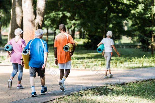 快乐的老年和多元文化养老金领取者拿着健身垫，在草地上<strong>散步</strong>的背景 