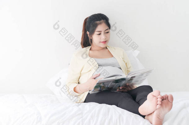 快乐亚洲孕妇在床上看书，生活方式概念.