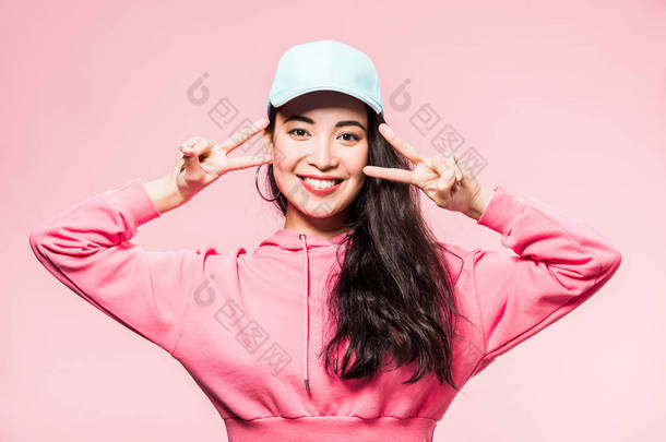 迷人的亚洲女人，身穿粉色套头衫，头戴一顶帽子，面带微笑，脸上挂着<strong>和平</strong>的红晕 
