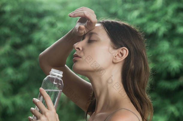 一位年轻女子在炎炎夏日喝瓶装水的户外肖像。水合物的概念。与热浪搏斗的<strong>女人</strong>. 