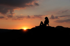 一个女孩坐在小山上落日的映衬下的剪影