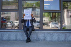 非洲美国商人阅读经济新闻报纸，而坐在办公楼附近玻璃门面