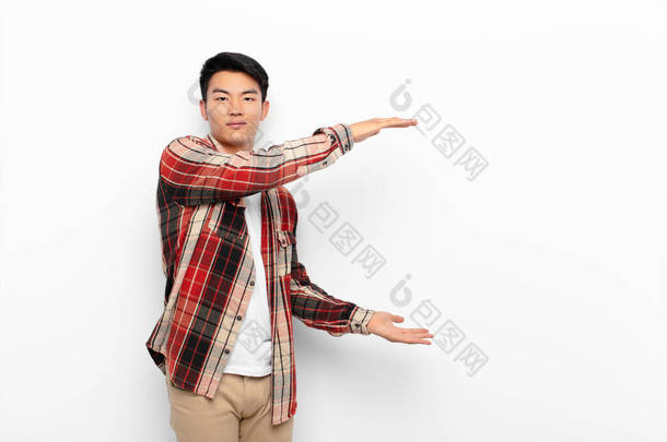 年轻的中国男人，双手放在侧边的复制空间上，用<strong>扁平</strong>的彩墙<strong>展示</strong>、提供或宣传一个物体