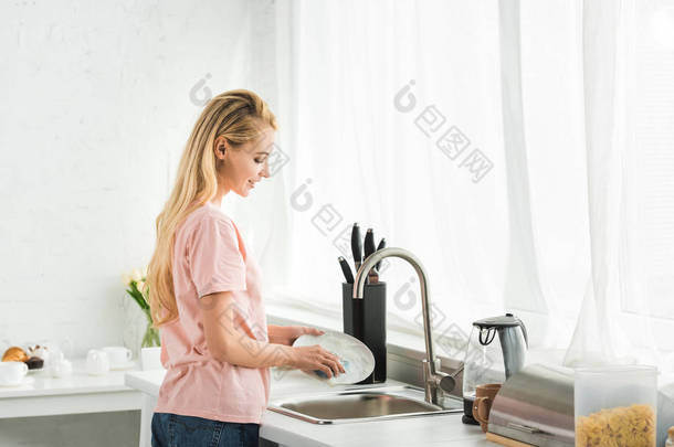 美丽的女人早上在厨房洗碗