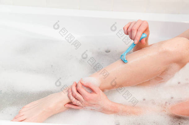 浴室里的女人用剃须刀刮腿。 用剃须刀拍手的特写.