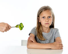 营养和健康饮食习惯为孩子健康饮食的概念。孩子不喜欢吃蔬菜。小可爱的女孩拒绝吃健康的花椰菜蔬菜白色背景