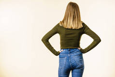 无法辨认的妇女站在向后穿苗条适合蓝色牛仔裤和卡其色的顶部, 白色背景与复制空间.