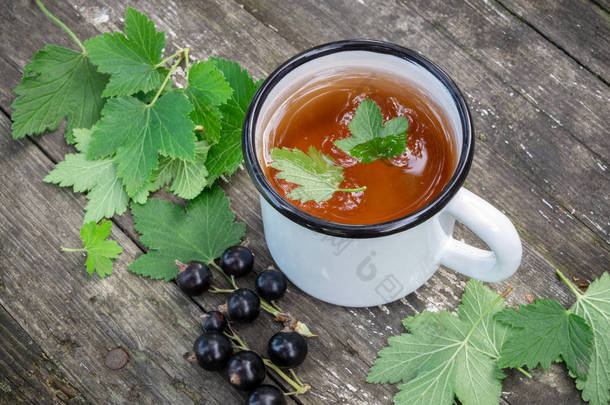 在户外木桌上有黑色醋栗浆果的搪瓷杯。顶部视图.