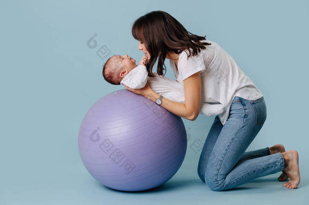 快乐的母亲做练习与她的婴儿婴儿在紫色瑜伽球