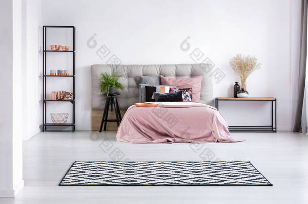 现代卧室内部地板上的黑色和白色<strong>地毯</strong>, 配有舒适的床、床头板、柔和的粉色床上用品和工业家具