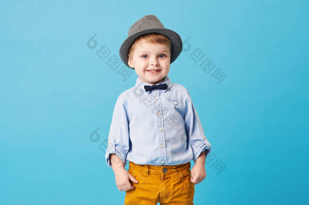 在<strong>蓝色背景</strong>中孤立的快乐快乐的小男孩的肖像。<strong>幼儿</strong>在帽子和时尚西装微笑, 并有乐趣 