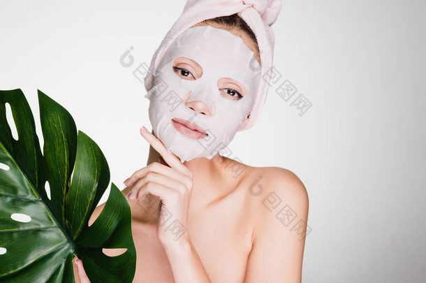 女人用毛巾在她的头上应用一个洁面面具在她的脸上灰色背景