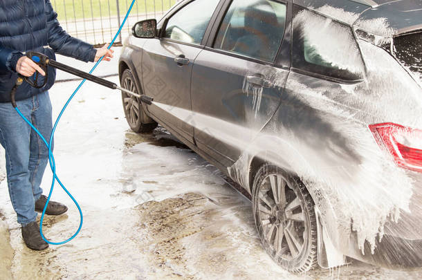 男人洗车。 使用高压水和泡沫的清洗车
