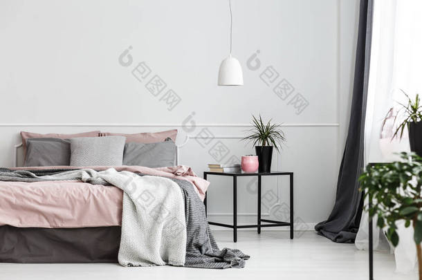温暖的毯子和灰色枕头在一张舒适的双人床与肮脏的粉红色板料由白色卧室内部的空的墙壁