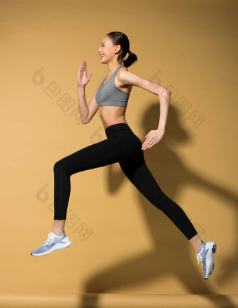亚洲身材纤细的女子练习热身伸展弹跳腿，工作室点亮黄色米黄色芥末背景阳光影印空间，概念女子可以做运动员运动6包图片
