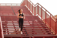 跑步运动员，穿着黑色运动服，紧身裤和上衣，适合快乐的女孩，跑下楼梯进行有氧训练，慢跑锻炼减肥。保健概念、户外运动