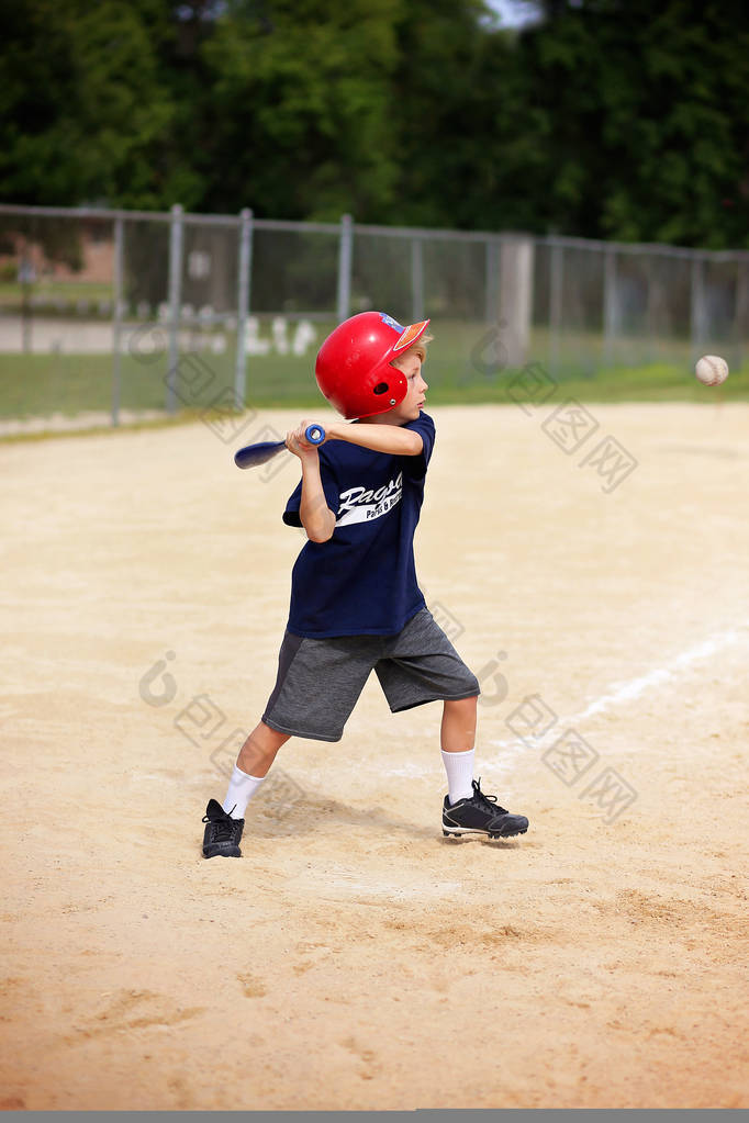 一个8岁的小男孩戴着头盔, 在一个小镇的青年 ragball 游戏中挥舞着棒球棍。.