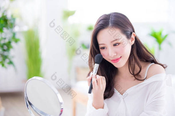 微笑的妇女与化妆刷靠近面对和镜子在家里