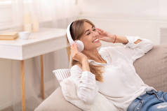 耳机中的妇女聆听躺在室内的 Sofa 上的音乐
