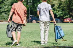 两个背着背包在公园草坪上行走的小学生的背景