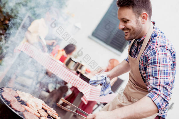 夏天的乐趣。年轻人烹调肉在烧烤为夏天家庭晚餐在后院.