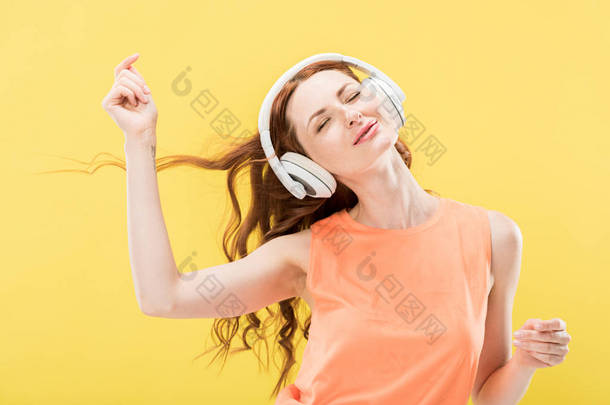 迷人的微笑红发女人在耳机里听音乐,用闭着的眼睛在黄色上跳舞