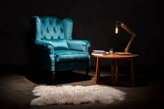 动物皮地毯、木制桌子、黑色灯具旁边有枕头的雅致天鹅绒蓝色扶手椅
