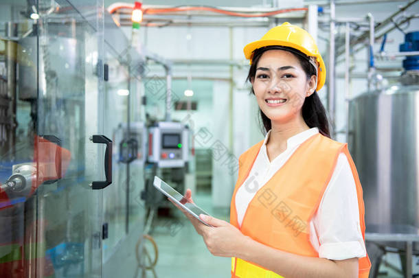 年轻工程师检查生产线。年轻美丽的中国妇女在安全帽持有片剂与瓶灌装生产线的背景下.