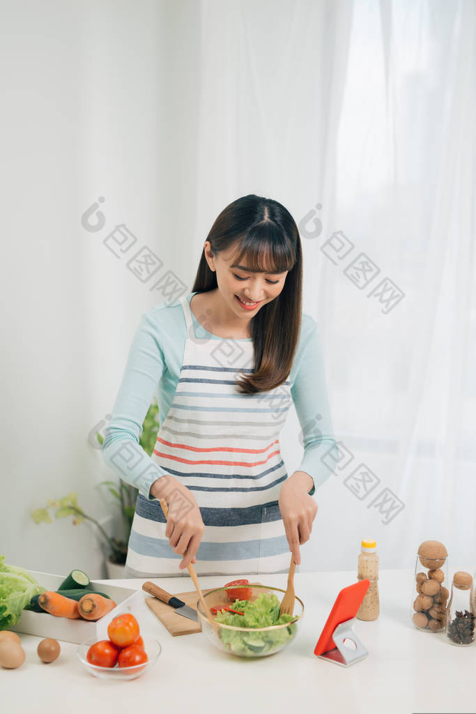 烹饪妇女看着手机，同时在厨房准备食物