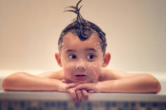 欢快的男孩与湿头发看着远离在浴缸