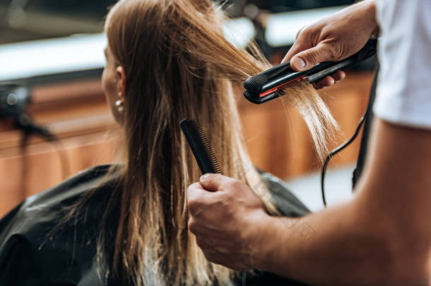 剪断的发型师持有梳子和使用发直器在美容院 
